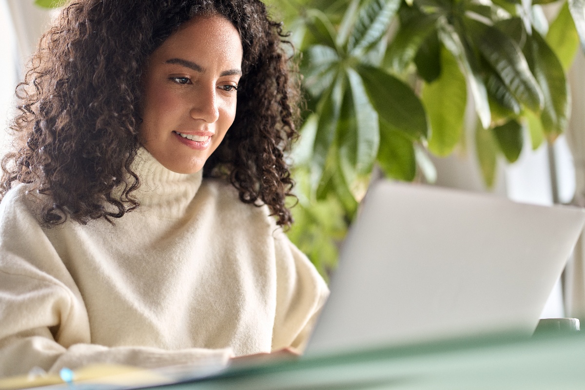  A young woman sitting at a desk and smiling while she uses her laptop. 