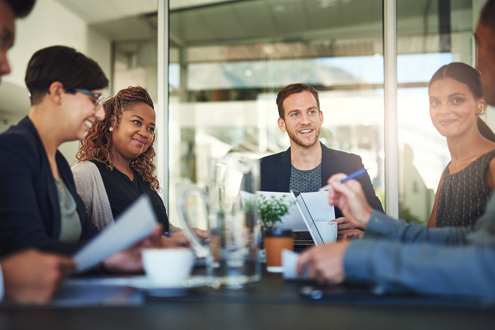 A diverse group of employees meet in a conference room. 