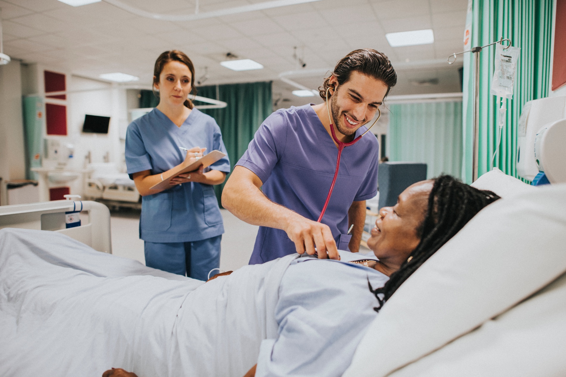 A male nurse uses a stethoscope to listen to a female patient's heartbeat. 