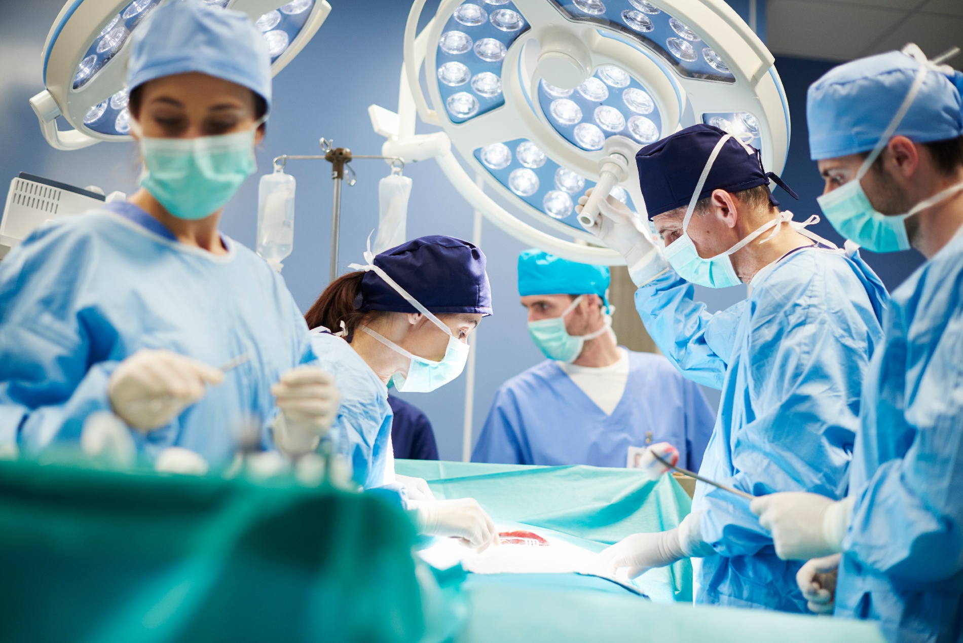 Two surgeons and three surgery assistants operate on a patient in an operating room. 