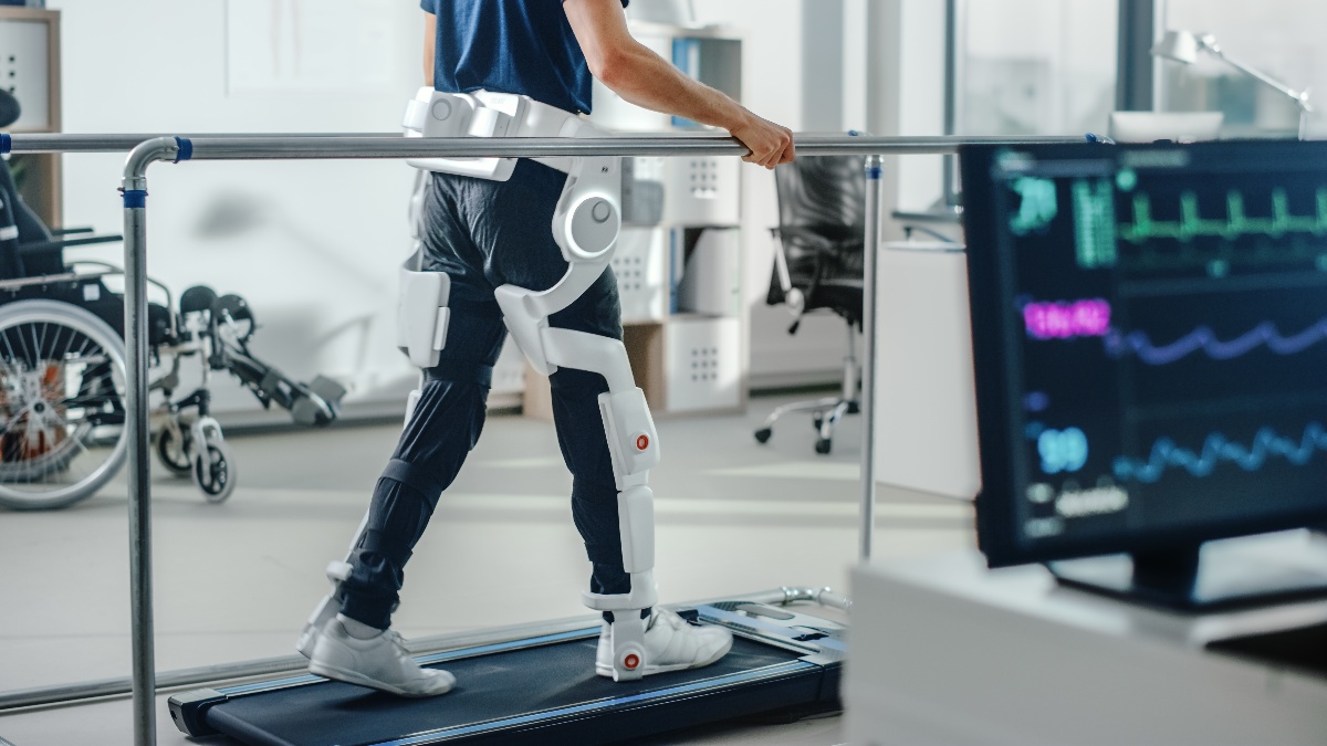 A man in a physical therapy facility walking on a treadmill with the help of a robotic walking assistance device. 