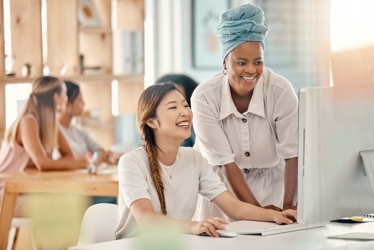 Two diverse co-workers look at a desktop computer together in an office.