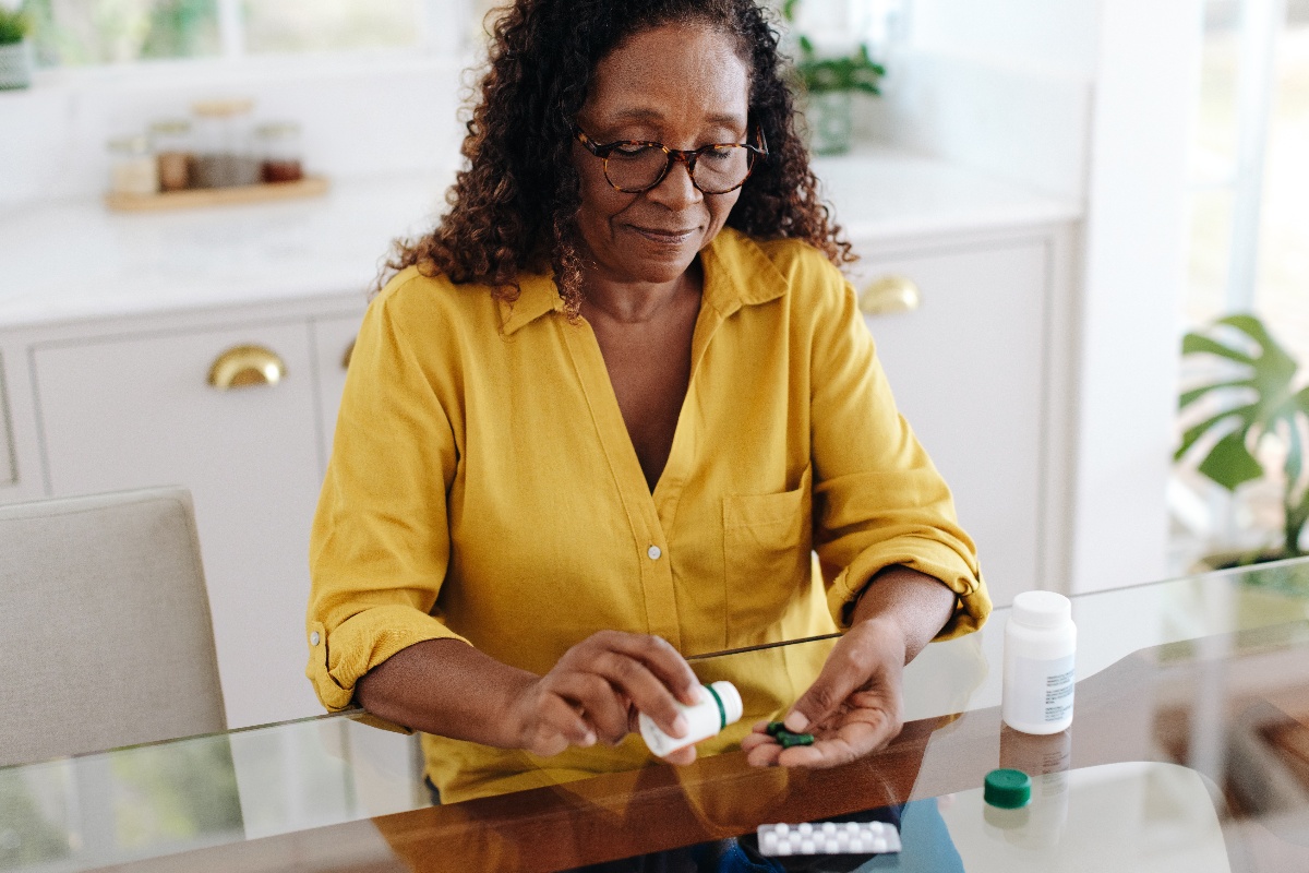 A woman with a chronic health condition takes medication while sitting at a desk. 